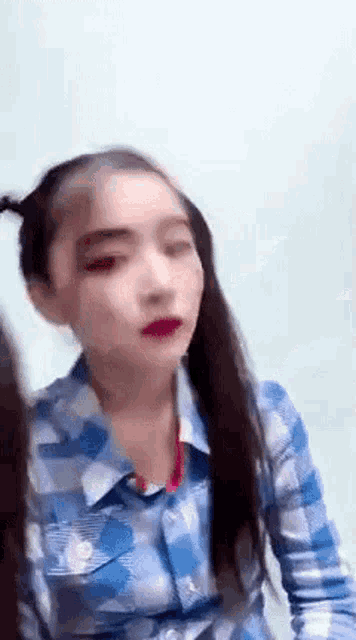the girl is wearing a plaid shirt and red lipstick and has pigtails .
