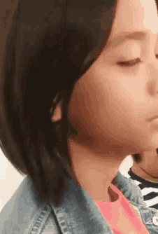 a close up of a girl 's face with her eyes closed wearing a denim jacket .