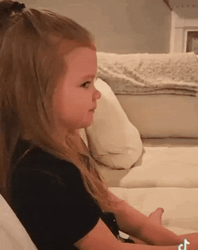 a little girl is sitting on a couch and making a face .