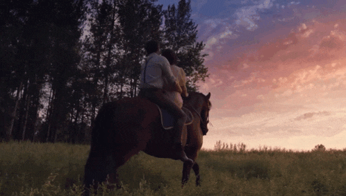 a man and woman riding a horse in a field