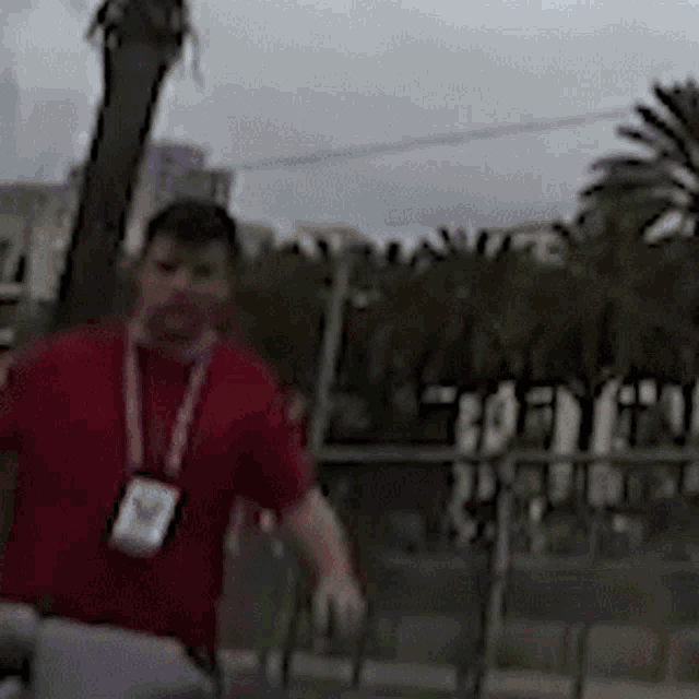 a man in a red shirt with a lanyard around his neck is standing in a park .
