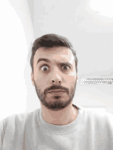 a man with a beard is making a funny face while wearing a white shirt .