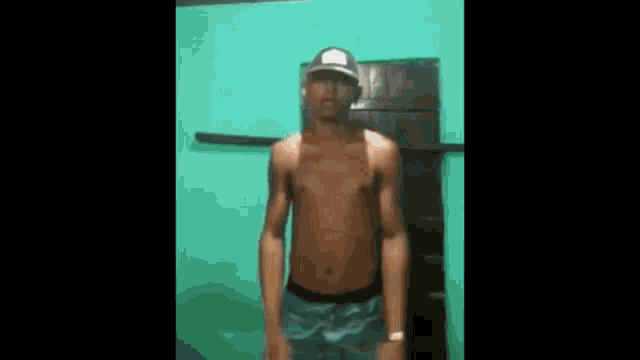 a shirtless man wearing a hat and shorts is standing in front of a door .