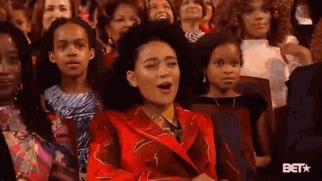 a woman in a red jacket is sitting in a crowd of people laughing .