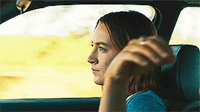 a woman is driving a car and looking out the window .