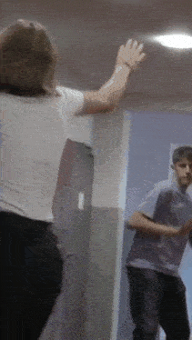 a woman in a white shirt is standing next to a man in a purple shirt in a hallway .