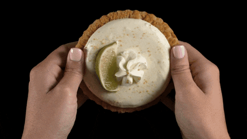 a person is holding a key lime pie with whipped cream and a lime slice on top
