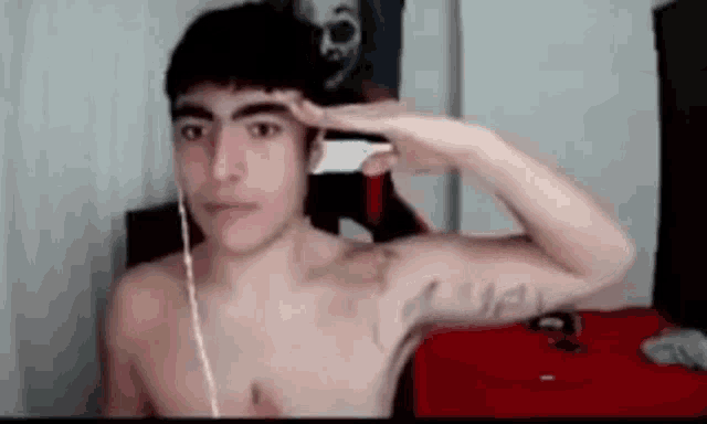 a shirtless young man is saluting while wearing headphones and taking a picture of himself .
