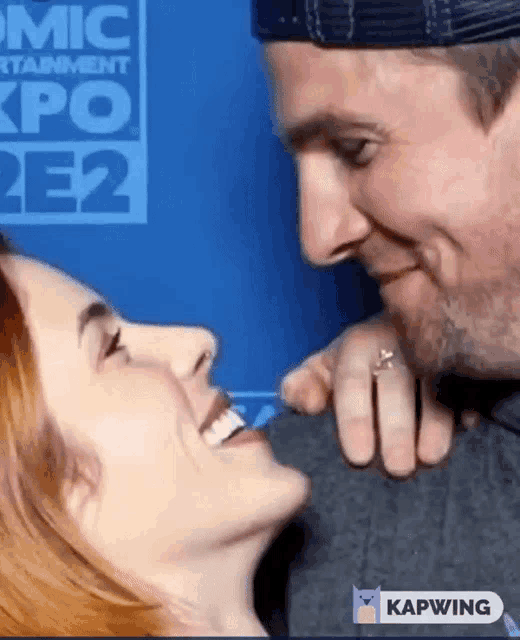 a man and woman are kissing in front of a sign that says comic expo 2e2 .