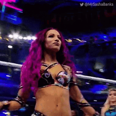 a woman with pink hair is standing in a wrestling ring with her arms outstretched .