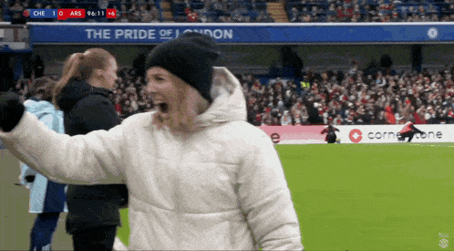 a woman stands on a soccer field with a banner that says the pride of london