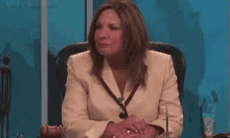 a woman in a suit is sitting in a chair with her hands folded in front of a blue wall .