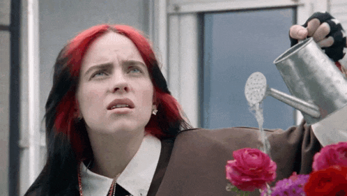 a woman with red hair is watering roses with a watering can .