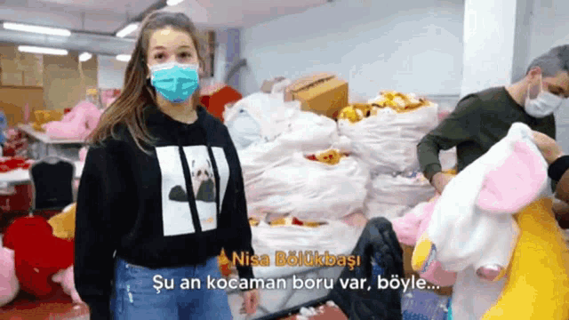 a woman wearing a mask stands in front of a pile of stuffed animals and says nisa bolukbasi