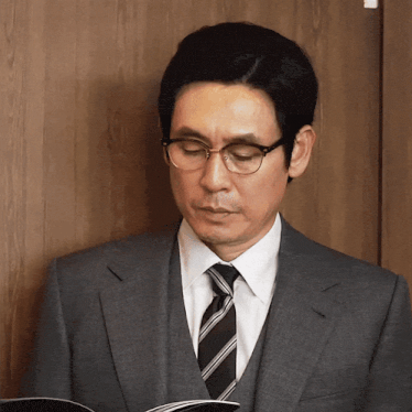 a man wearing glasses and a suit looks down at something