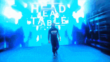a man wearing a gtc shirt walks in front of a large screen
