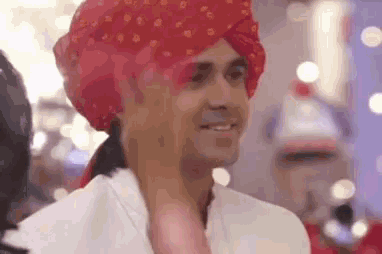 a man wearing a red turban is smiling while standing in a room .