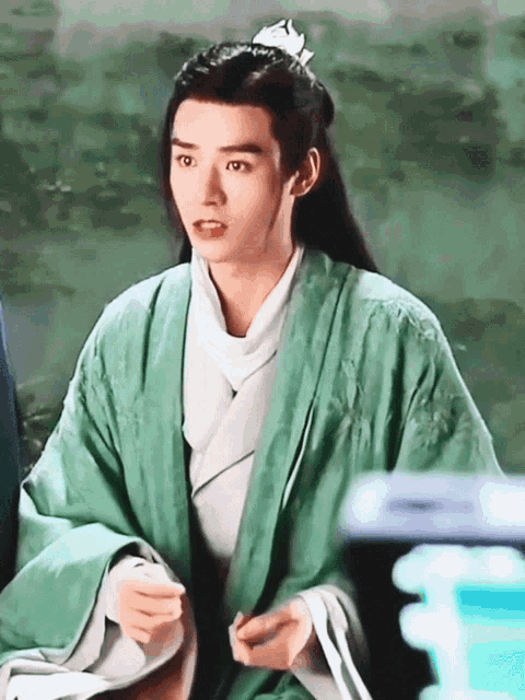 a man wearing a green robe and a white shirt has a flower in his hair