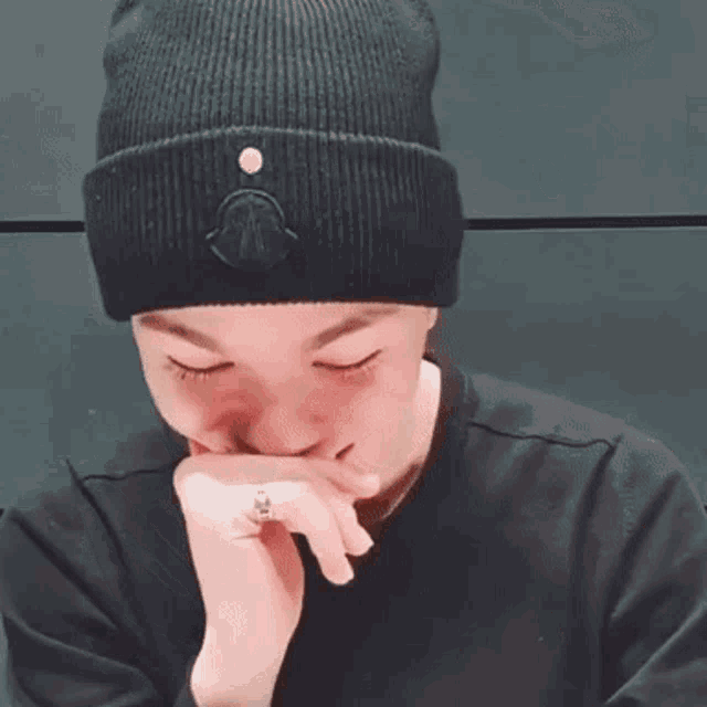 a person wearing a black beanie and a black sweater is covering their mouth .