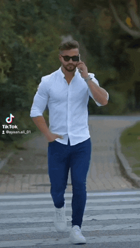a man in a white shirt and blue jeans is talking on his phone