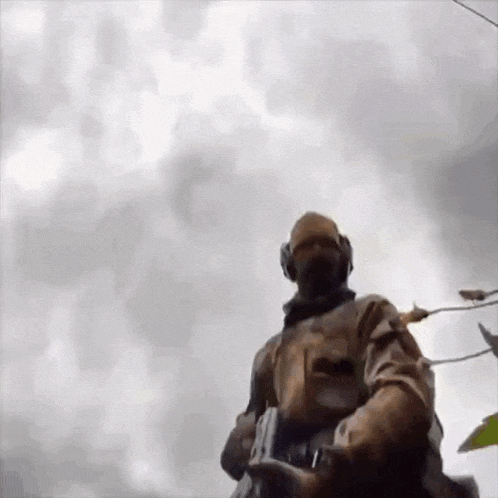 a soldier is standing in front of a cloudy sky holding a rifle .