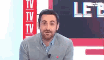 a man with a beard is standing in front of a tv screen with the word tv on it .