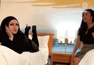 a woman in a hijab is laying on a bed while another woman sits on a bed .