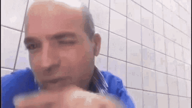 a man in a blue shirt is eating a sandwich in a bathroom .