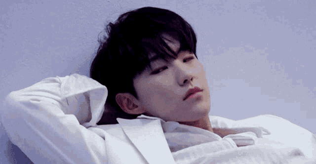 a young man in a white shirt is laying down with his head on his arms .