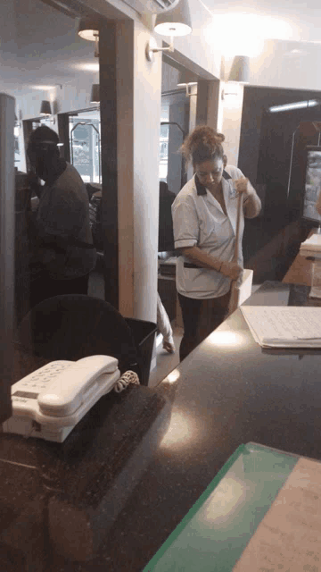 a woman standing at a counter with a phone on it that says ' telephone '