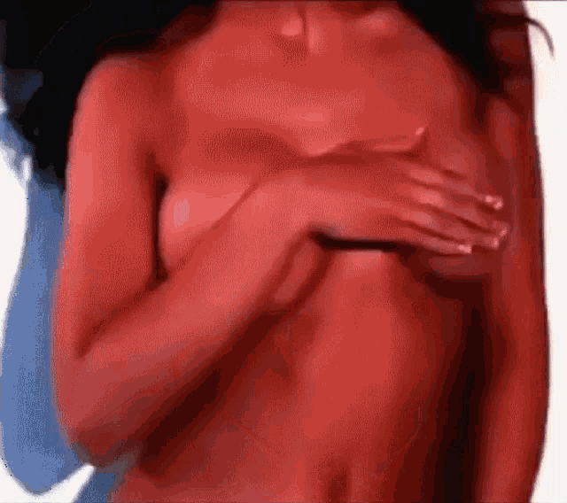 a naked woman with red skin is holding her breasts with her hands .