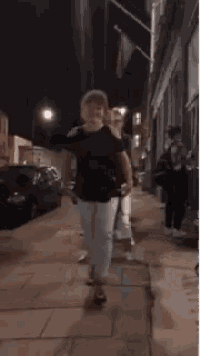 a woman is dancing on a sidewalk in front of a group of people .