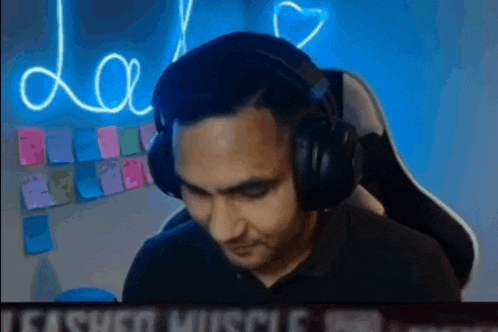 a man wearing headphones is sitting in front of a neon sign that says " love "