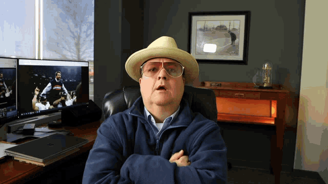 a man wearing a hat and glasses is sitting in front of a computer monitor