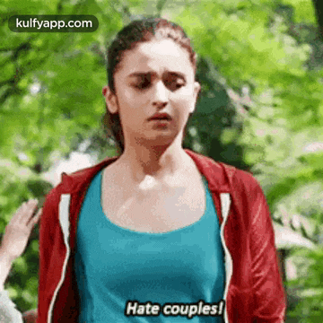 a woman in a blue tank top and a red jacket is standing in the woods and says `` hate couples '' .