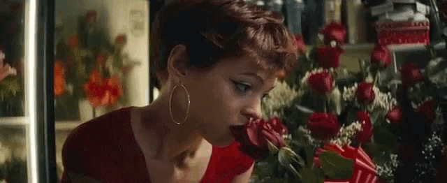 a woman in a red dress is smelling a bouquet of roses
