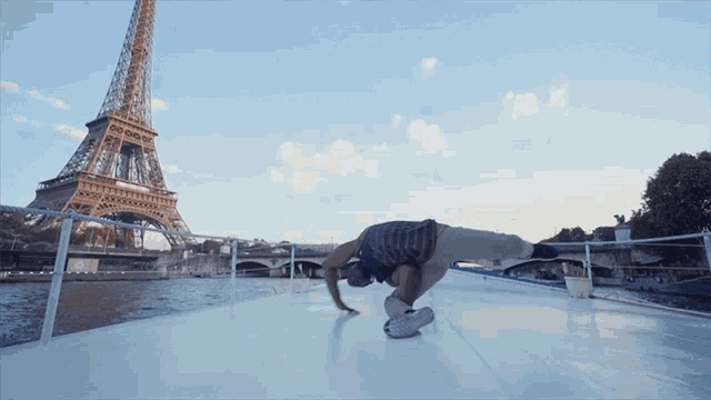 a man is doing a handstand on a boat in front of the eiffel tower