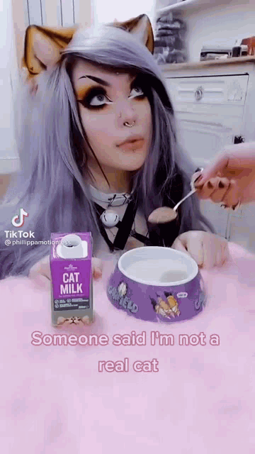 a woman with cat ears is sitting at a table with a bowl of cat milk and a carton of cat milk .