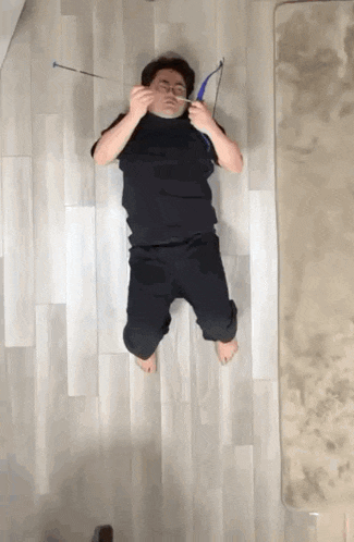 a man is laying on the floor with a bow and arrow in his face .