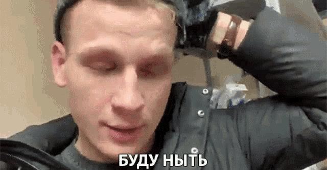 a man wearing a hat and a jacket is talking in a foreign language while holding his hand to his head .