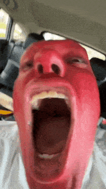 a man with a red face is screaming in a car with his mouth wide open .