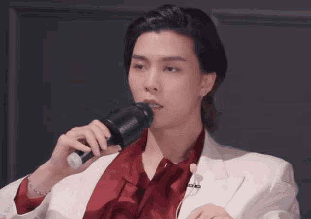 a man wearing a white jacket and a red shirt is holding a microphone