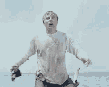 a man in a muddy shirt is holding a camera in his hand and making a funny face .
