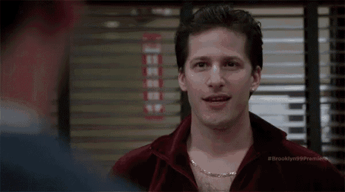 a man is wearing a red robe and a gold chain around his neck while talking to another man .