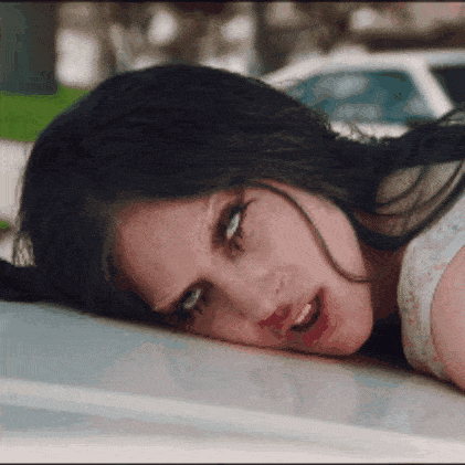 a woman is laying on the hood of a car and making a funny face