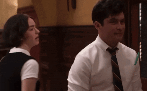 a man in a white shirt and tie sits next to a girl in a black vest