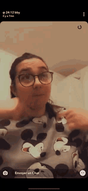 a woman wearing glasses and a mickey mouse shirt is taking a selfie