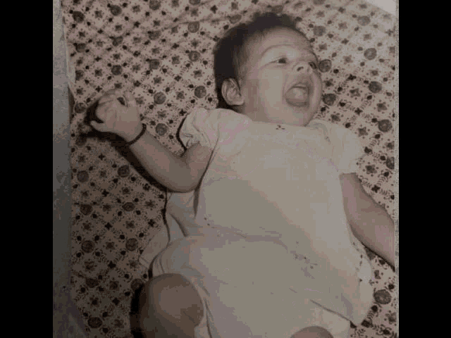 a baby in a white dress laying on a bed