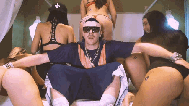 a man in sunglasses is surrounded by women in bikinis and one of them has a tattoo on her butt