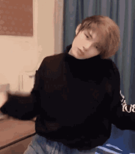 a young man wearing a black turtleneck sweater is dancing in a room .